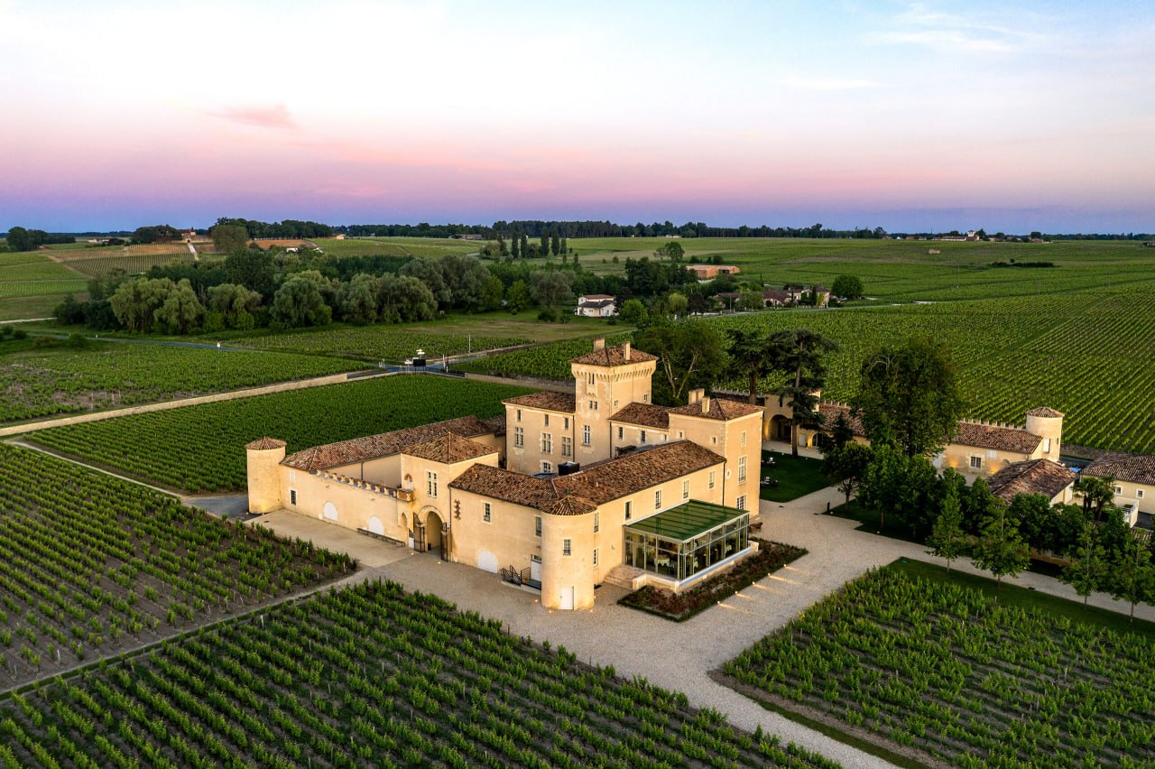 Aerial view of a grand Bordeaux château surrounded by vineyards at dusk